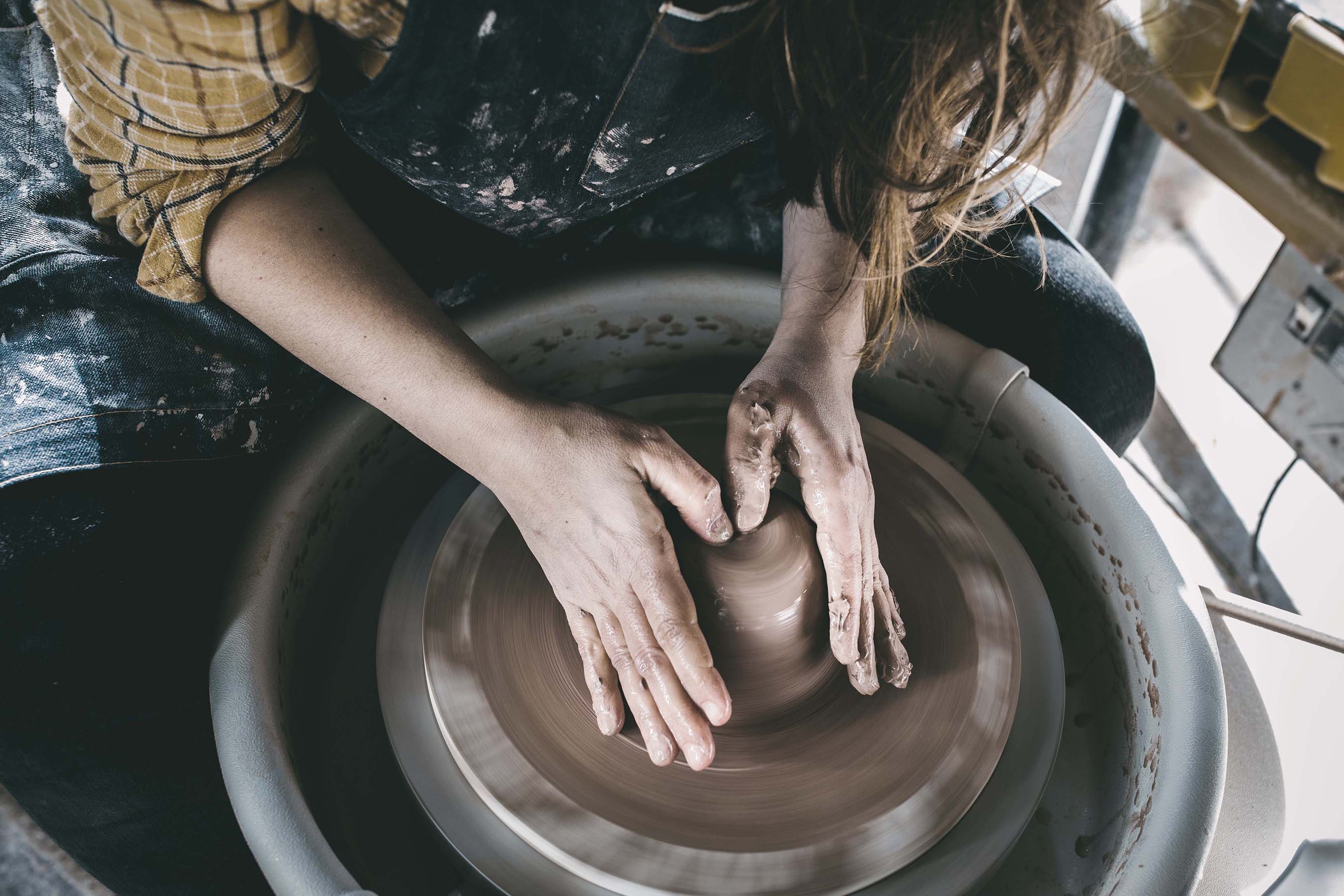 person making a mug on a pottery wheel with red clay