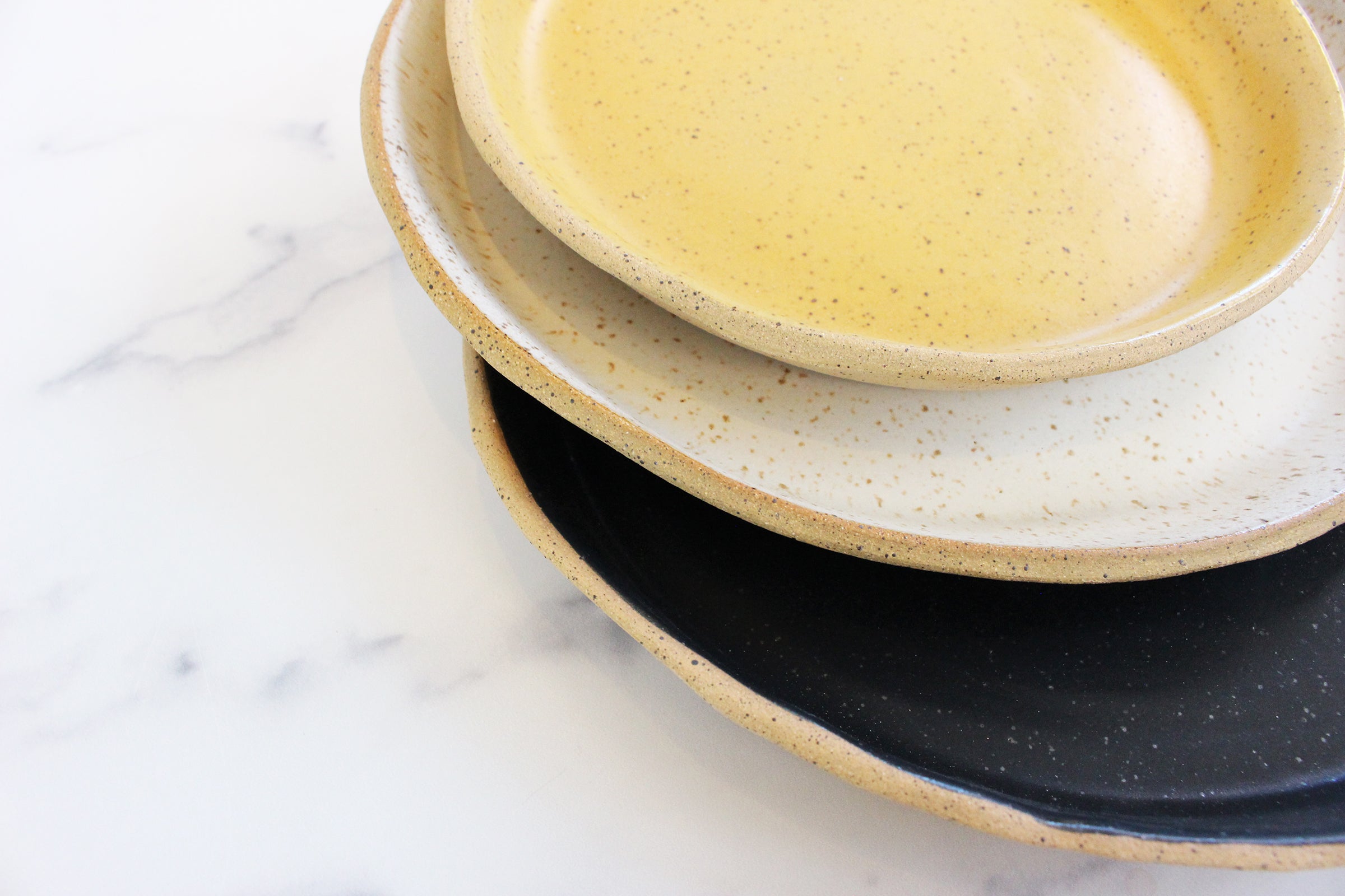 set of three pottery dinner plates in a variety of colors, black, white, and yellow dishes